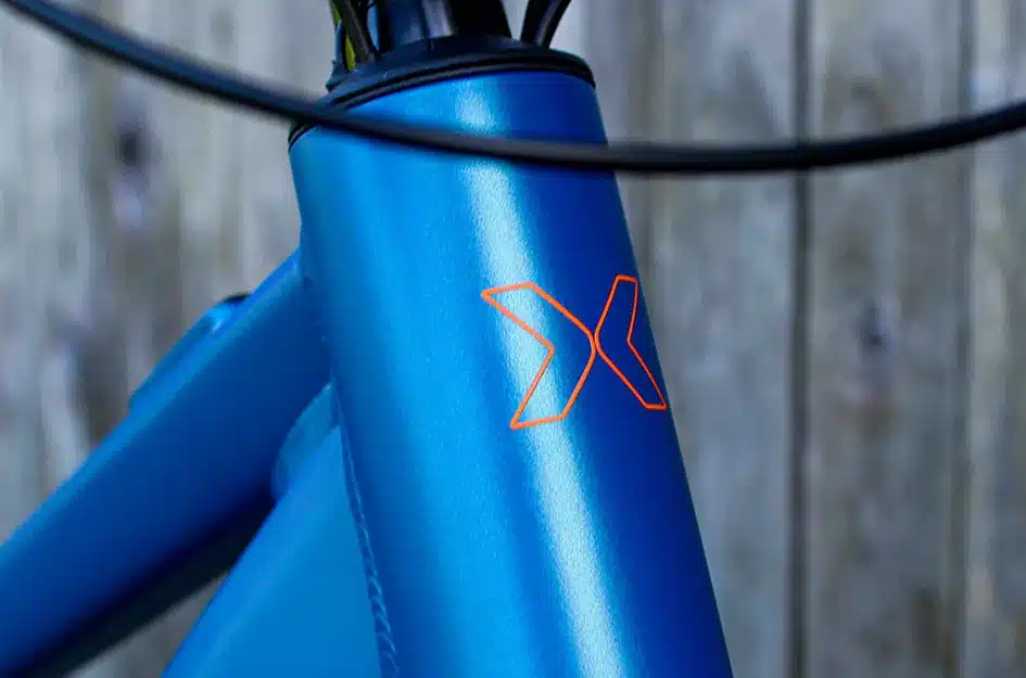 Nahaufnahme des blauen Fahrradrahmens des MAXX Racemaxx ELF Tour mit orangefarbenem
