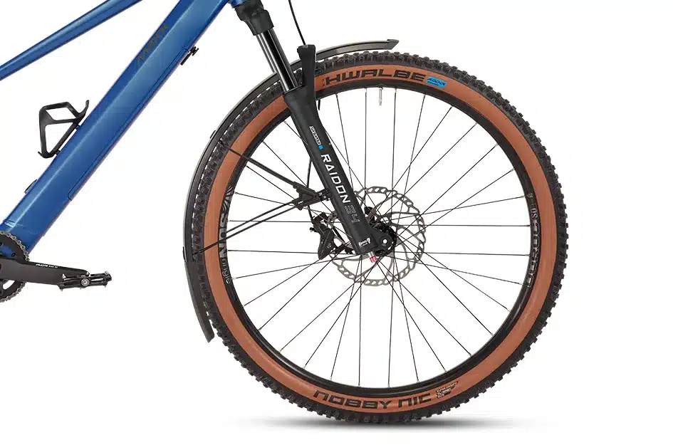 Detailaufnahme eines blauen MAXX Racemaxx ELF Tour E-Trekkingbikes mit Fokus auf das Vorderrad, die schwarze Federgabel mit der Aufschrift 'RAIDON 34', den braunen Reifen 'Schwalbe Nobby Nic' und den Schutzblechen.