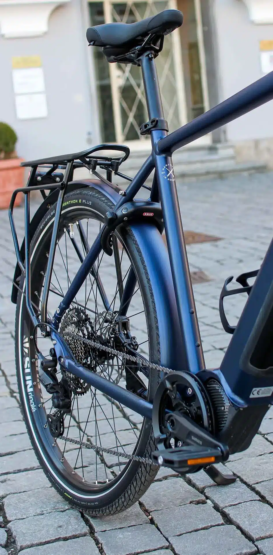 Nahaufnahme des blauen E-Trekkingbikes MAXX Crossmaxx ELS, Fokus auf Hinterrad, Kassette, Kette und das Unterrohr mit dem integrierten Motor.