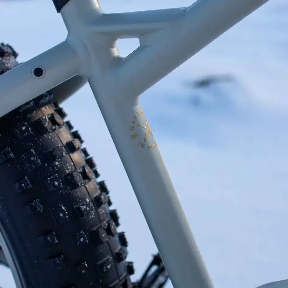 Nahaufnahme des Rahmens mit der Aufschrift 'Handmade in Germany' und des profilierten Reifens eines MAXX Jagamoasta ELS SH, das im Schnee steht.