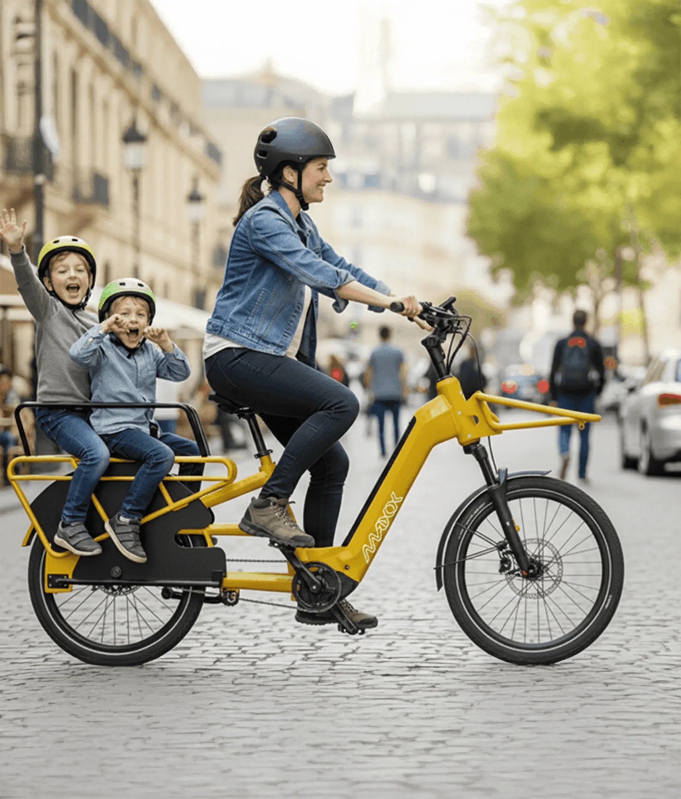 Frau fährt mit zwei Kindern auf einem gelben Maxx Maxximo Urban Longtail-E-Bike auf einer Kopfsteinpflasterstraße.