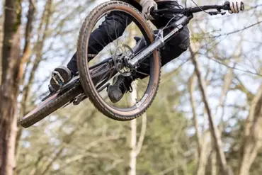 Ein Mann mit Helm und Sonnenbrille fährt mit einem Mountainbike durch die Luft auf einem Waldtrail.