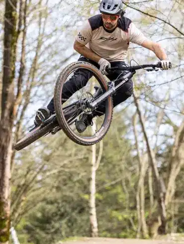 Ein Mann mit Helm und Sonnenbrille fährt mit einem Mountainbike durch die Luft auf einem Waldtrail.