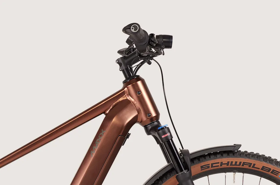 Detailaufnahme des vorderen Rahmens eines braunen MAXX Pacemaxx ELS Sport E-Bikes mit Federgabel, Lenker und Teil des Vorderrads mit Schwalbe-Reifen.