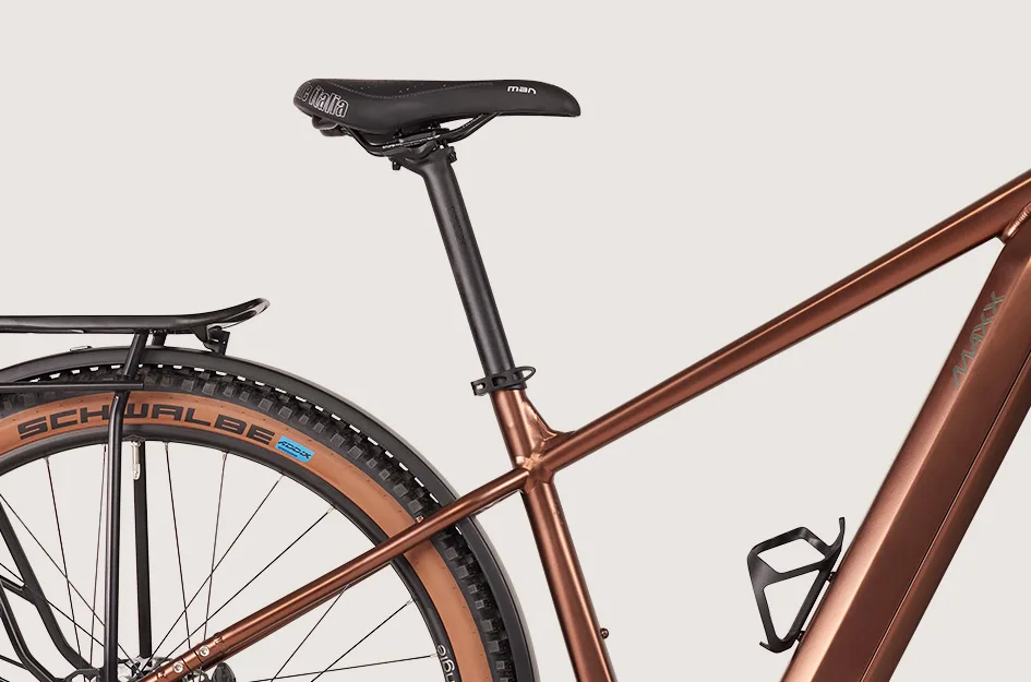 Nahaufnahme eines MAXX Pacemaxx ELS Sport Fahrradrahmens in Kupferbraun, Fokus auf das Hinterrad mit Schwalbe Reifen, Gepäckträger, Sattelstütze und Wasserflaschenhalter. Das Fahrrad ist ein E-Hardtail mit Offroad-Anleihen.