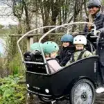 Familie mit drei Kindern in einem Winther Cargoo 2+2 Lastenrad, gesteuert von einer Frau.