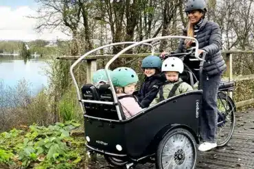Familie mit drei Kindern in einem Winther Cargoo 2+2 Lastenrad, gesteuert von einer Frau.