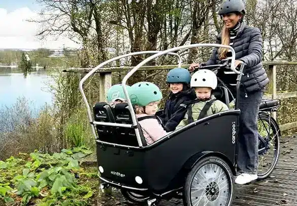 Familie mit drei Kindern in einem Winther Cargoo 2+2 Lastenrad, gesteuert von einer Frau.
