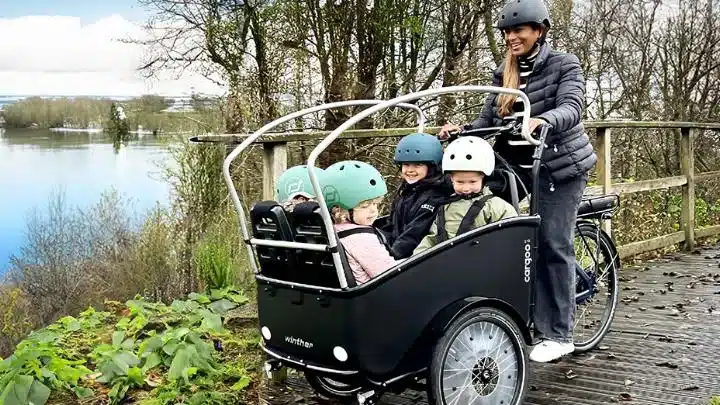 Familie mit drei Kindern in einem Winther Cargoo 2+2 Lastenrad, gesteuert von einer Frau.