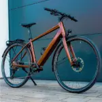 Ein MAXX Roadmaxx ELF Tour E-Bike in Braun steht seitlich vor einer dunklen Garagentür.