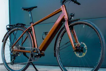 Ein MAXX Roadmaxx ELF Tour E-Bike in Braun steht seitlich vor einer dunklen Garagentür.