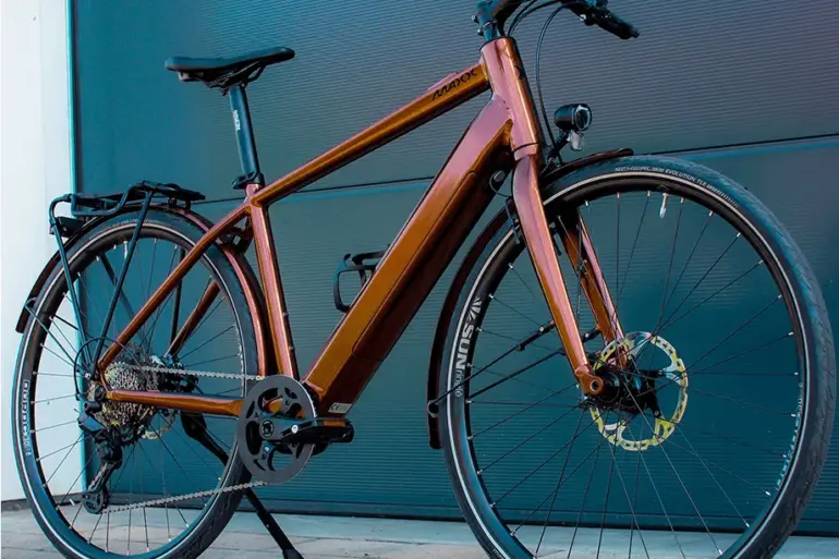 Ein MAXX Roadmaxx ELF Tour E-Bike in Braun steht seitlich vor einer dunklen Garagentür.