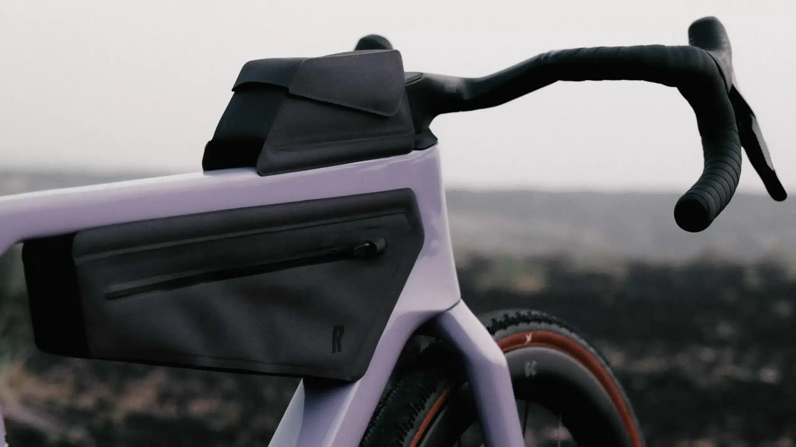 Nahaufnahme eines lila Gravelbikes mit schwarzen integrierten Taschen am Rahmen und Oberrohr sowie einem schwarzen Lenker