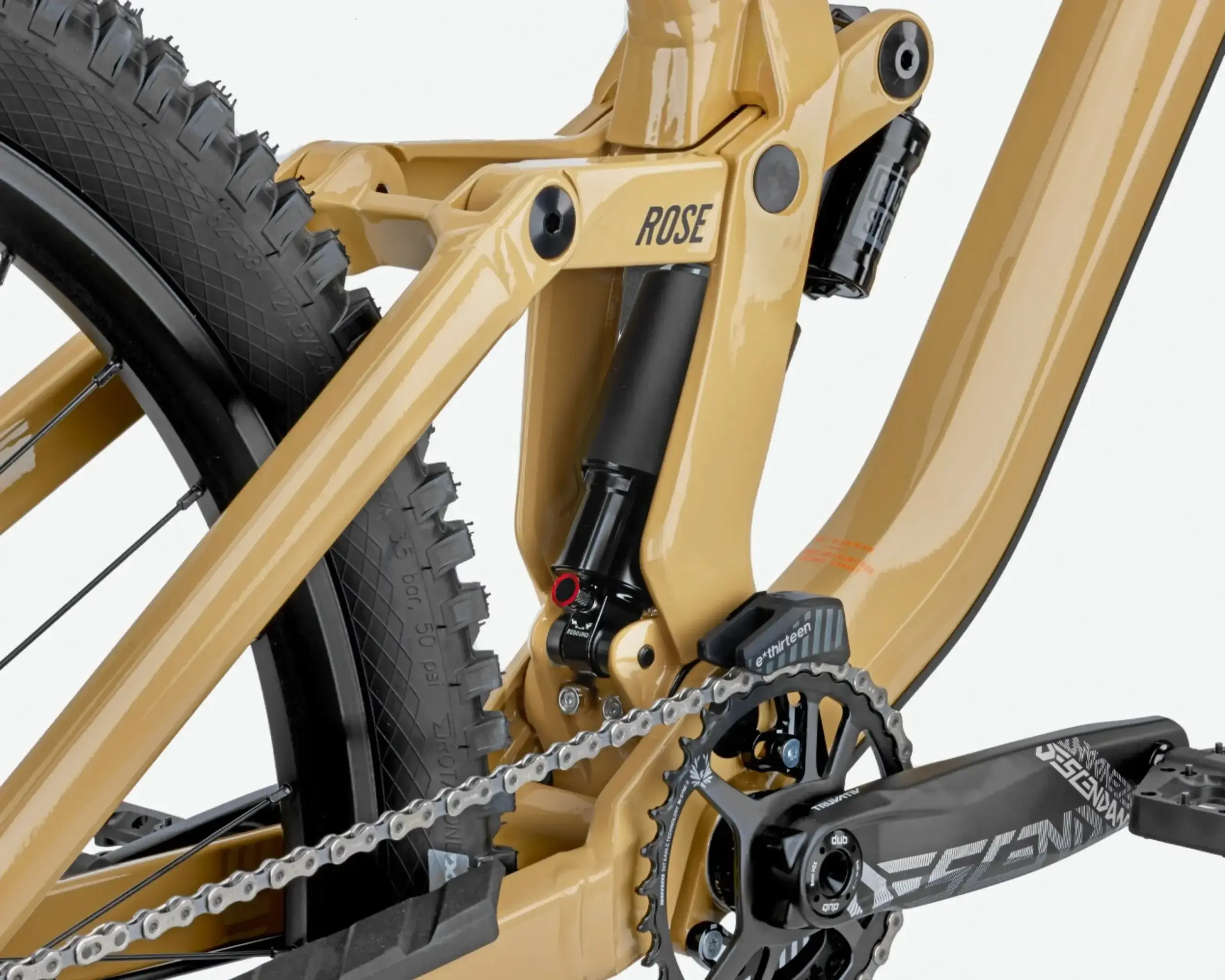 Detailaufnahme des Hinterbaus eines goldenen Rose Scrub SC Freeride-Mountainbikes mit sichtbarem Dämpfer, Kette, Kettenblatt und Hinterradnabe.