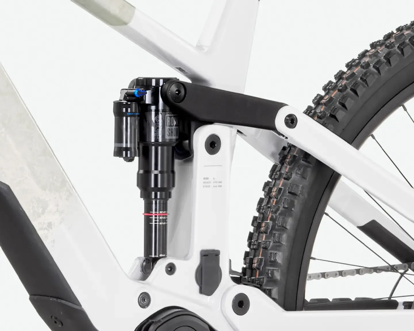 Detailaufnahme des Hinterbaus eines weißen E-Mountainbikes mit schwarzem Dämpfer und markantem Reifenprofil, die Federungselemente und Rahmenkonstruktion zeigend.