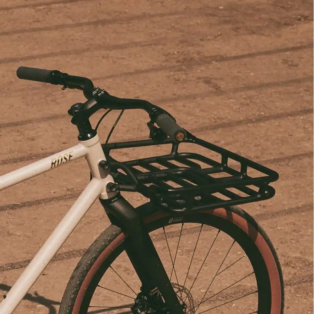 Vorderansicht eines beigefarbenen ROSE Hobo Fahrrads mit schwarzem Frontgepäckträger, schwarzem Lenker und Reifen mit roten Seitenwänden.