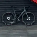 Graues Carbon-Rennrad mit 50mm hohen Aero-Laufrädern, das vor einer dunklen horizontalen Wand mit einer roten Treppe steht.