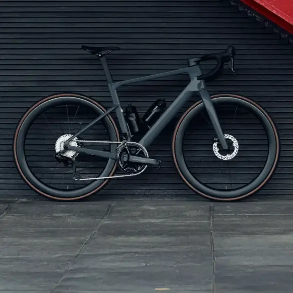 Graues Carbon-Rennrad mit 50mm hohen Aero-Laufrädern, das vor einer dunklen horizontalen Wand mit einer roten Treppe steht.