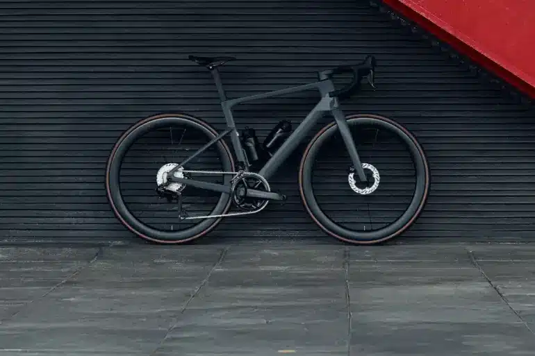 Graues Carbon-Rennrad mit 50mm hohen Aero-Laufrädern, das vor einer dunklen horizontalen Wand mit einer roten Treppe steht.