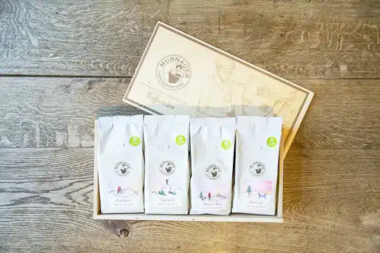 Vier Packungen Outdoor-Kaffee von Murnauer Kaffeerösterei im Präsentkarton auf Holztisch.
