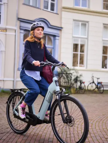 Eine Frau mit Helm fährt ein hellgrünes Batavus E-Bike auf einer gepflasterten Straße.