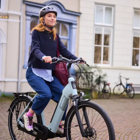 Eine Frau mit Helm fährt ein hellgrünes Batavus E-Bike auf einer gepflasterten Straße.
