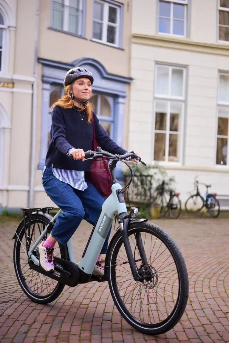 Eine Frau mit Helm fährt ein hellgrünes Batavus E-Bike auf einer gepflasterten Straße.
