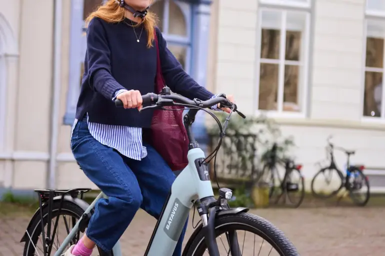 Eine Frau mit Helm fährt ein hellgrünes Batavus E-Bike auf einer gepflasterten Straße.