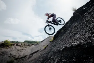 Ein Mountainbiker mit Helm und sportlicher Kleidung fährt mit seinem E-Bike über einen steilen, felsigen Hang und springt in der Luft.