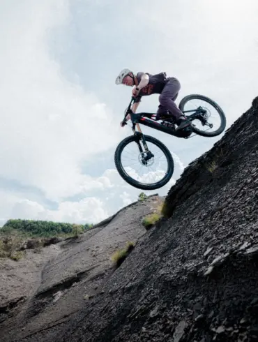 Ein Mountainbiker mit Helm und sportlicher Kleidung fährt mit seinem E-Bike über einen steilen, felsigen Hang und springt in der Luft.