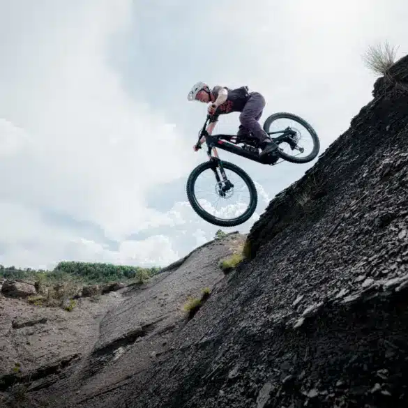 Ein Mountainbiker mit Helm und sportlicher Kleidung fährt mit seinem E-Bike über einen steilen, felsigen Hang und springt in der Luft.