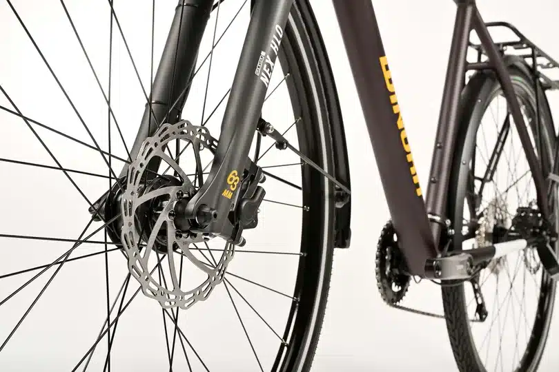 Nahaufnahme des vorderen Teils eines dunklen Winora Domingo X20 Fahrrads, mit Fokus auf die Speichen, die Scheibenbremse, die SR Suntour NEX HLO Federgabel mit der Angabe 63mm und dem seitlichen Schriftzug