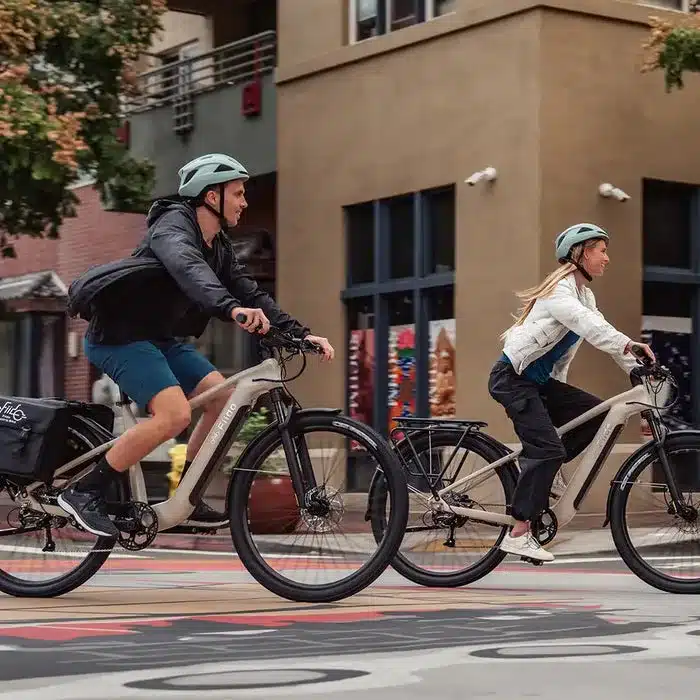 Ein Mann und eine Frau fahren nebeneinander auf Fiido Nomads E-Bikes durch eine Stadtstraße. Beide tragen Fahrradhelme und wirken entspannt.