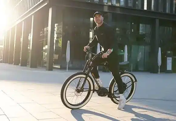 Mann fährt ein schwarzes Ruff Cycles Biggie E-Bike mit weißen Felgenlinien und breiten Reifen, aufrecht sitzend mit BMX-Lenker.