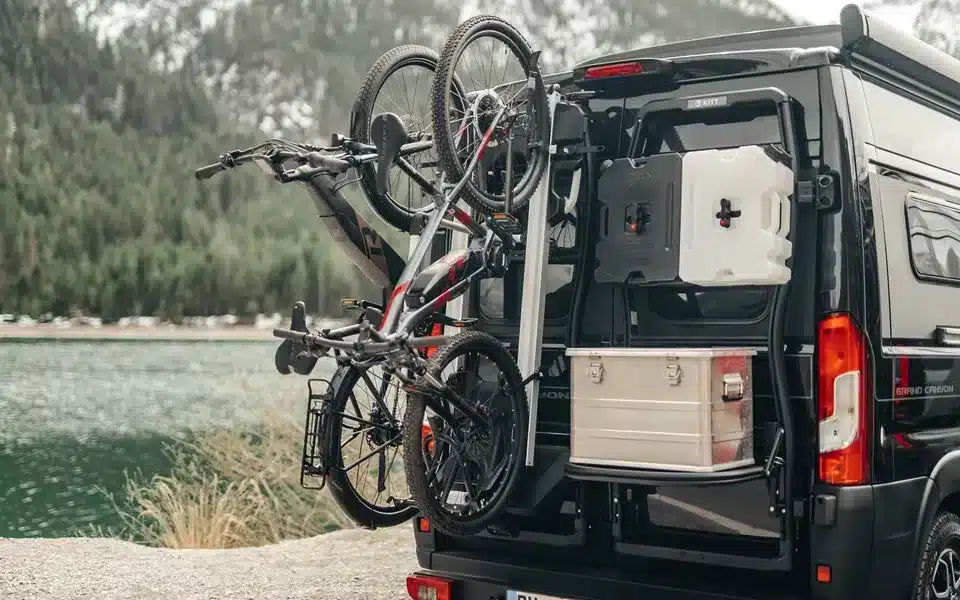 Bike Carrier Swing Fahrradträger mit zwei Fahrrädern am Heck eines Kastenwagens auf einem Stellplatz vor Bergkulisse.