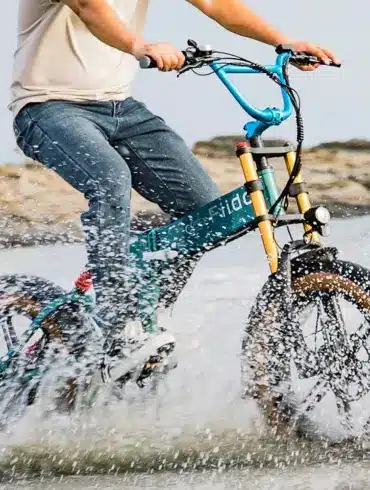 Fahrradfahrer fährt ein grünes Fiido M1 Pro Fatbike durch spritzendes Wasser.