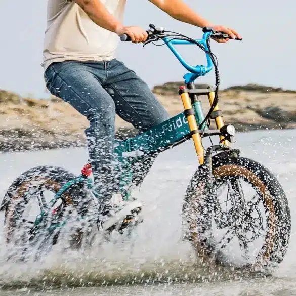 Fahrradfahrer fährt ein grünes Fiido M1 Pro Fatbike durch spritzendes Wasser.