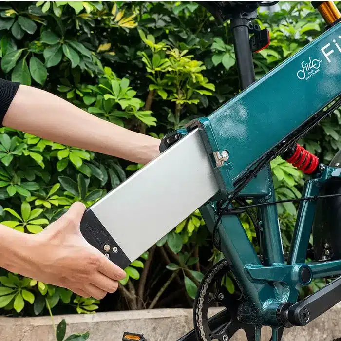 Person entnimmt den silbernen Akku eines grünen Fiido M1 Pro E-Bikes.