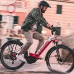 Mann mit Helm fährt ein rotes und weißes GASGAS E-Bike auf einer nassen Straße.