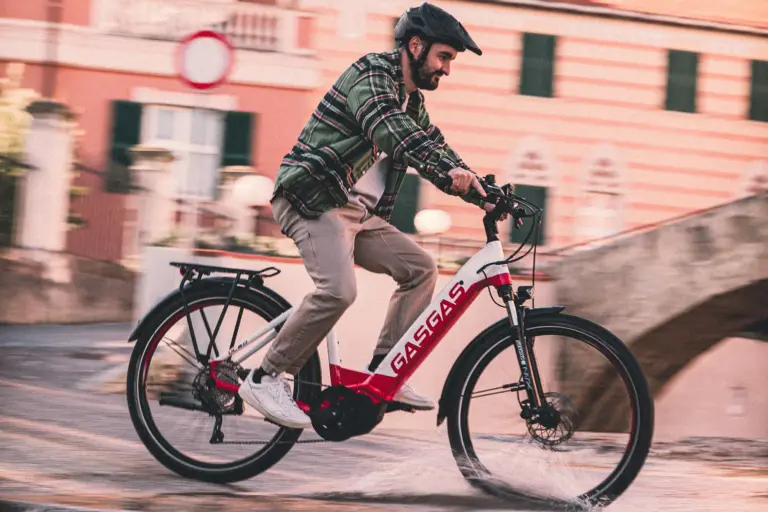 Mann mit Helm fährt ein rotes und weißes GASGAS E-Bike auf einer nassen Straße.