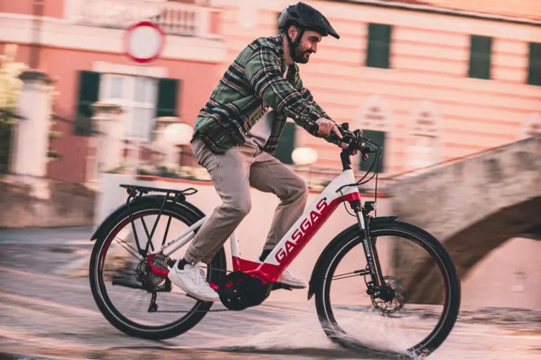 Mann mit Helm fährt ein rotes und weißes GASGAS E-Bike auf einer nassen Straße.