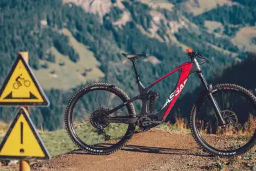 GASGAS ECC 4 E-Enduro Mountainbike in Blanca White mit roten Akzenten, stehend auf einem Feldweg in den Bergen. Im Vordergrund sind Warnschilder für Radfahrer zu sehen.