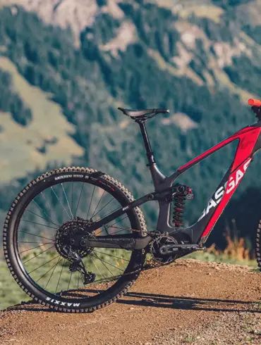 GASGAS ECC 4 E-Enduro Mountainbike in Blanca White mit roten Akzenten, stehend auf einem Feldweg in den Bergen. Im Vordergrund sind Warnschilder für Radfahrer zu sehen.