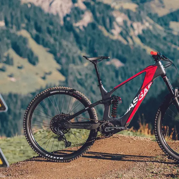GASGAS ECC 4 E-Enduro Mountainbike in Blanca White mit roten Akzenten, stehend auf einem Feldweg in den Bergen. Im Vordergrund sind Warnschilder für Radfahrer zu sehen.