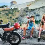 Ein Onemile Scrambler E-Bike steht neben einer Gruppe junger Leute, die auf einer Steinmauer sitzen und Wassermelone essen.