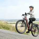 Frau mit Helm auf einem roten Dukawey FUGL3.0 City-E-Bike fährt auf einer Straße bergauf.