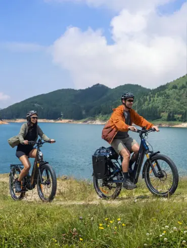 Ein Mann und eine Frau fahren nebeneinander auf ENGWE E26 3.0 Pro E-Bikes auf einem Feldweg neben einem See.