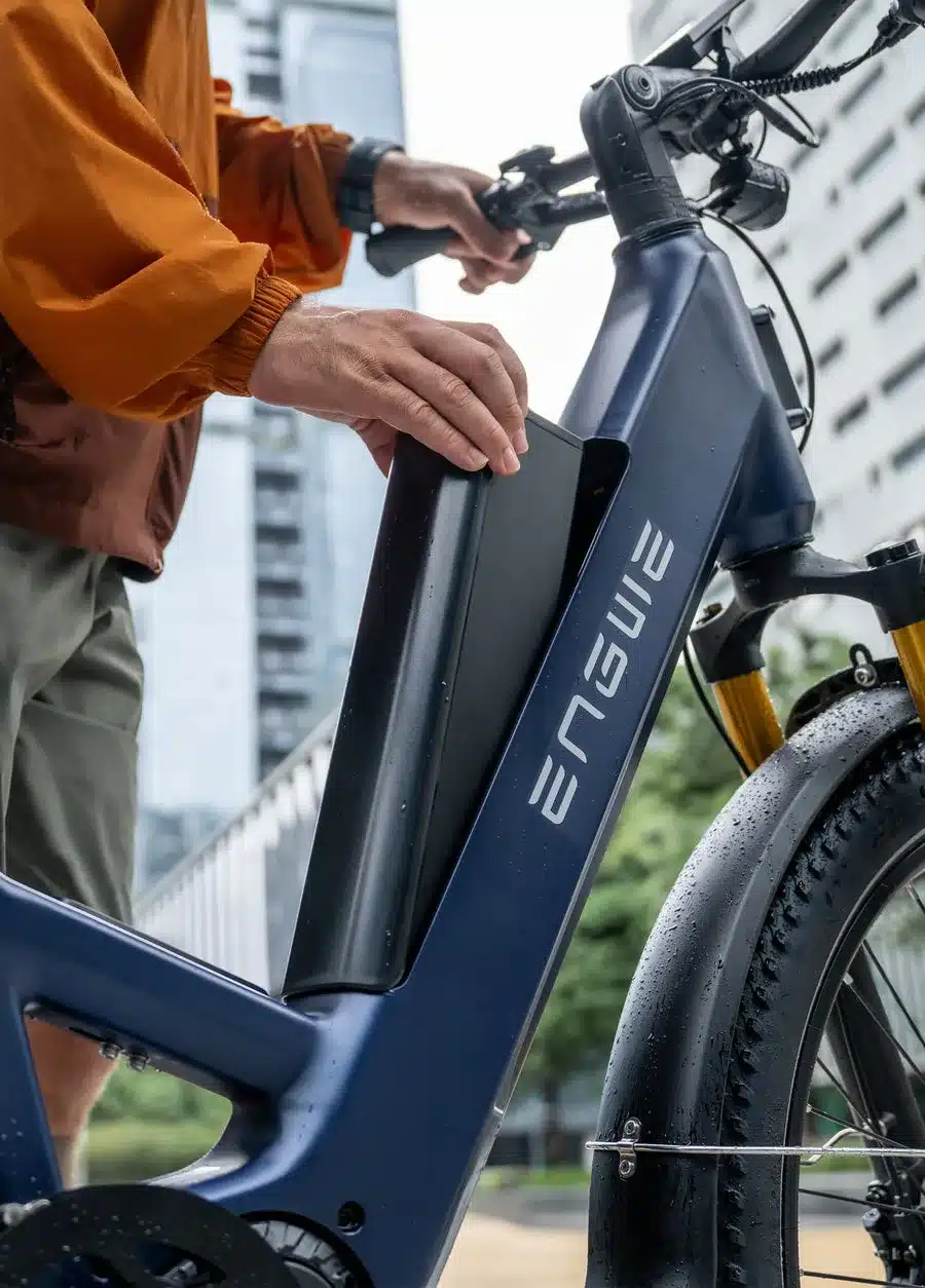 Person entnimmt den seitlich im blauen Rahmen integrierten Akku eines ENGWE E26 3.0 Pro E-Bikes.