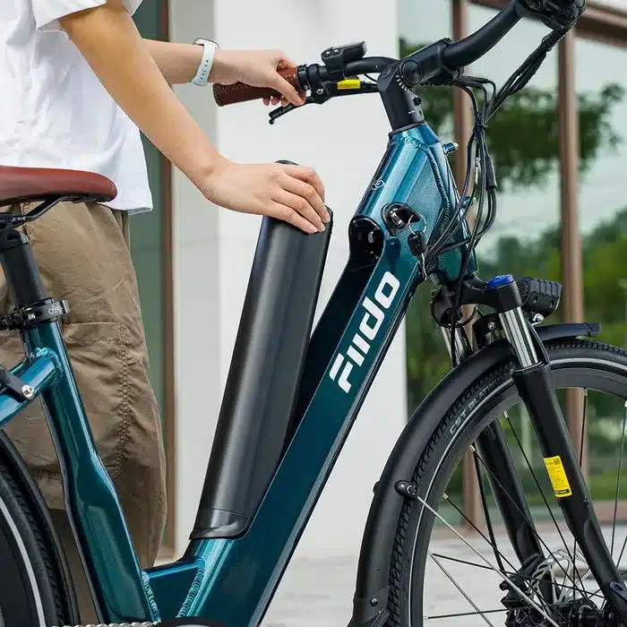 Nahaufnahme einer Person, die den Akku aus dem Rahmen eines teal-farbenen Fiido C11 Pro E-Bikes zieht. Der Fokus liegt auf der Hand, die den Akku greift, und dem unteren Teil des Rahmens.