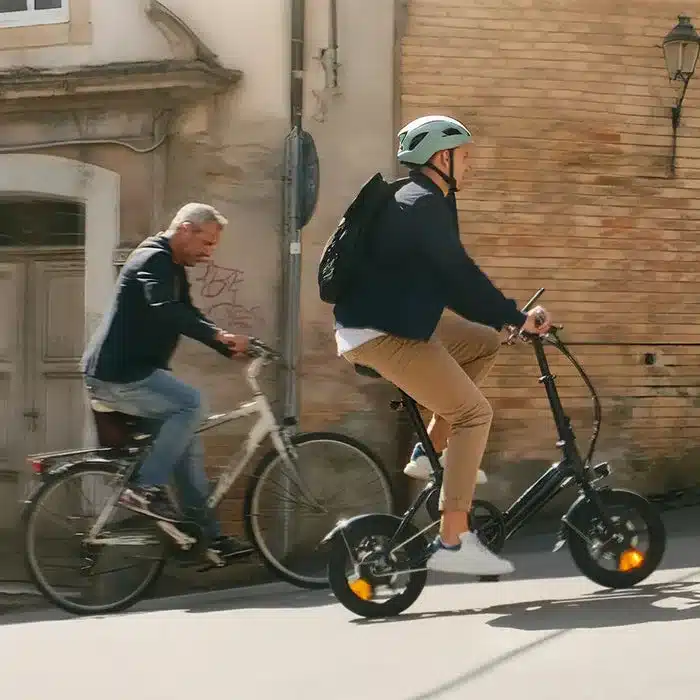 Ein Mann fährt ein schwarzes Fiido D3 Pro Mini E-Bike mit kleinen Rädern und Helm auf einer Straße, während ein anderer Mann auf einem größeren Fahrrad daneben fährt.